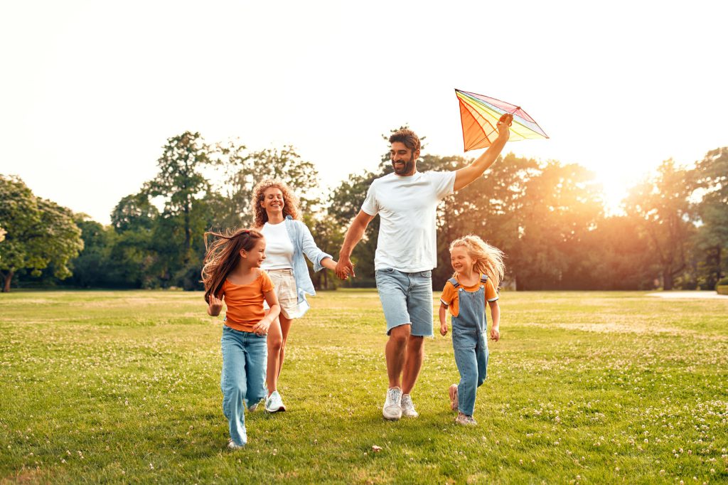 two adults and two children running outside to fly a kite